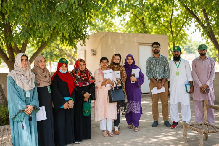 A FAME field enumeration team of nine women and three men outside a rural building, carrying identity lanyards, branded caps, questionnaires and clipboards.
